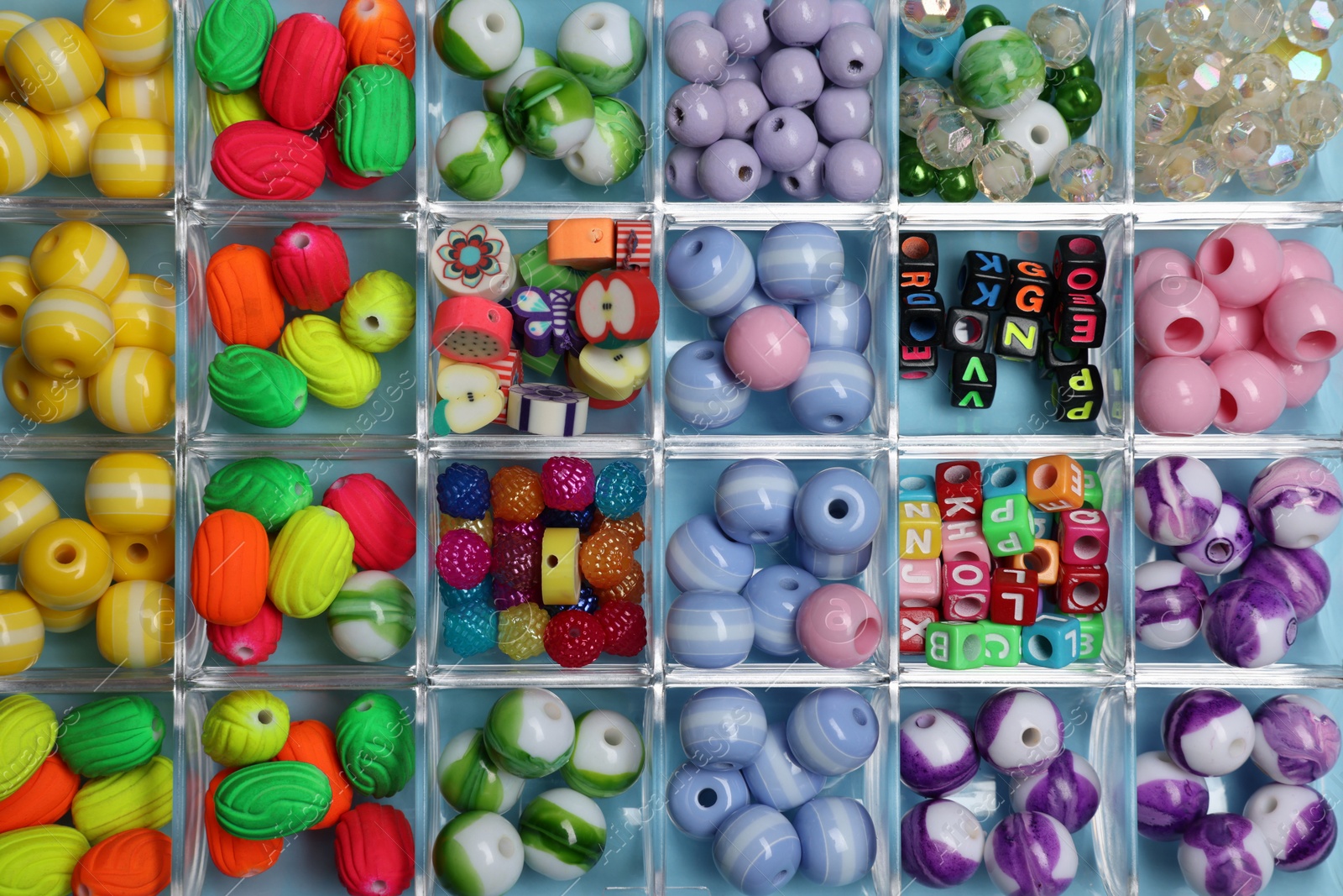 Photo of Box with different colorful beads on light blue background, top view