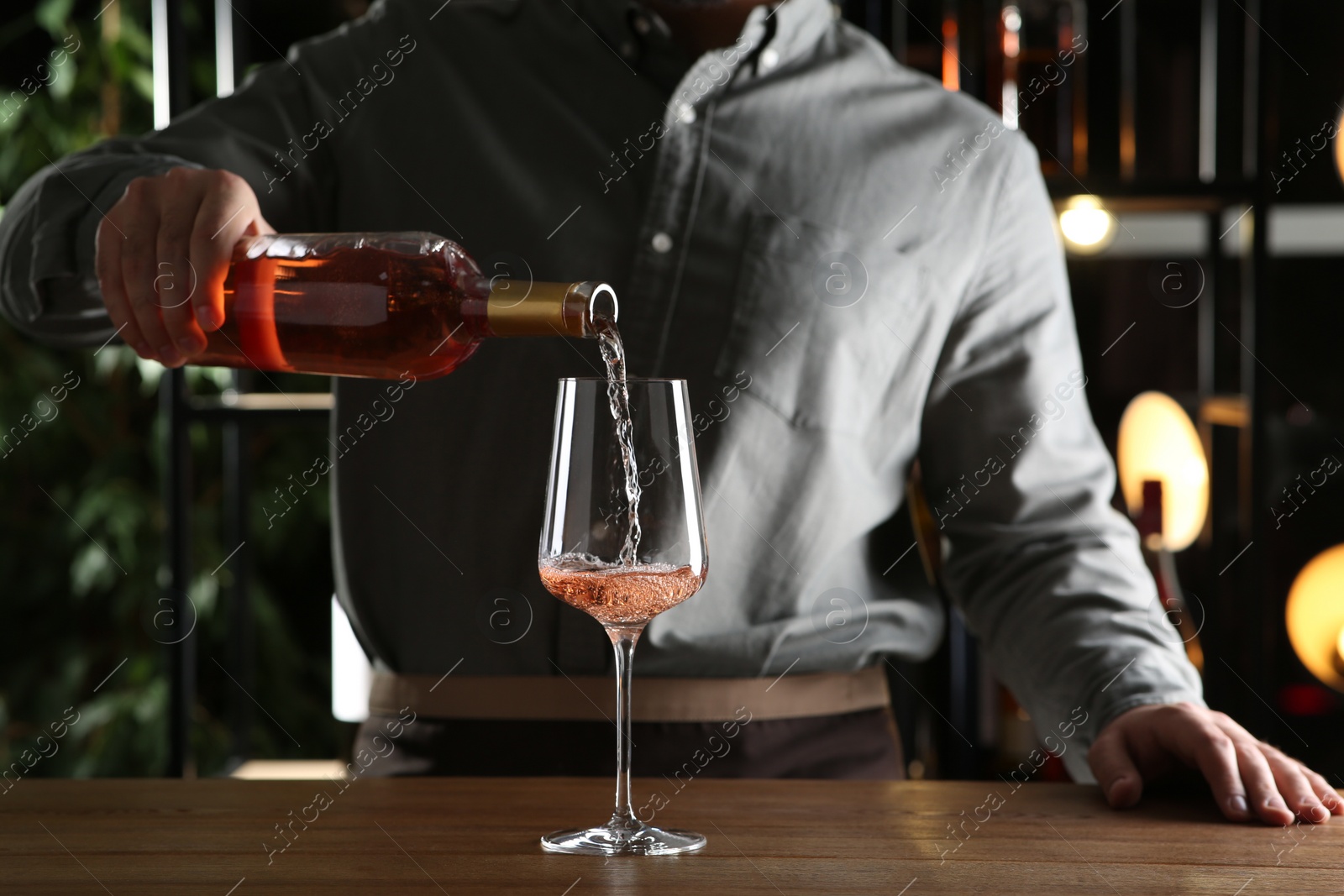 Photo of Man pouring rose wine from bottle into glass indoors, closeup