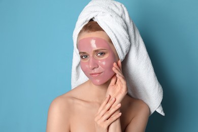Young woman with pomegranate face mask on light blue background