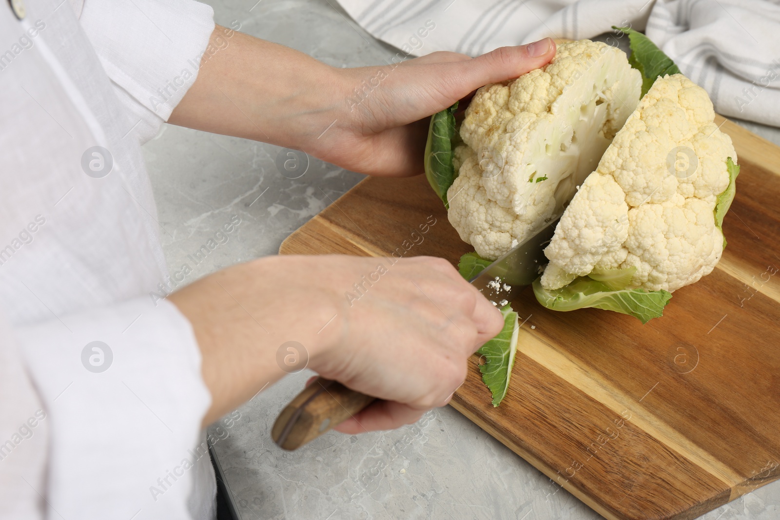 Photo of Woman cutting fresh cauliflower at light grey table, closeup