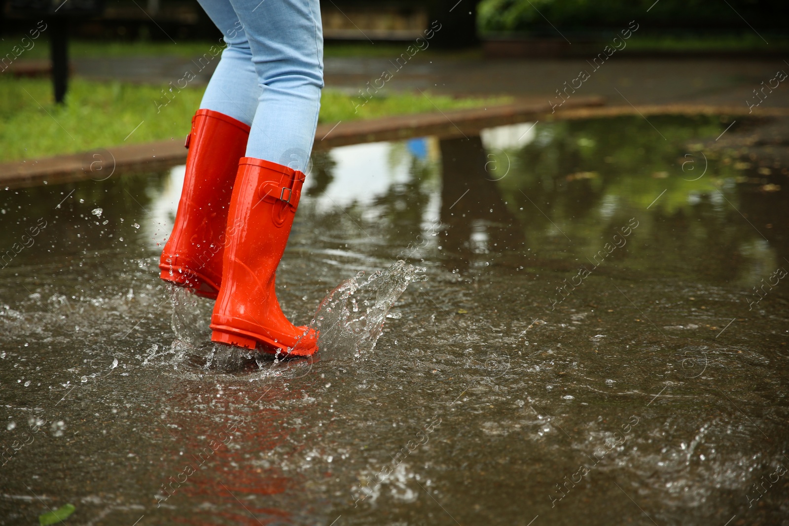 Photo of Woman with red rubber boots jumping in puddle, closeup. Rainy weather