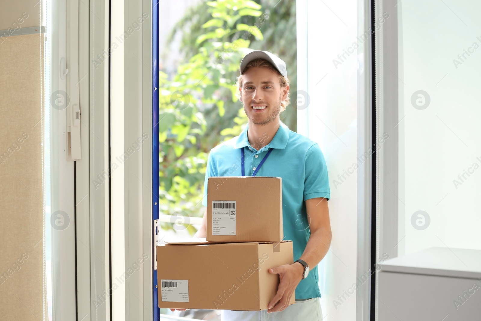 Photo of Young courier standing with parcels on doorstep