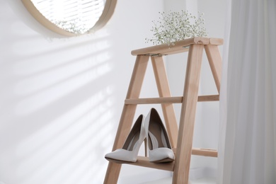 Photo of Beautiful wedding shoes on ladder and dress hanging in room, closeup