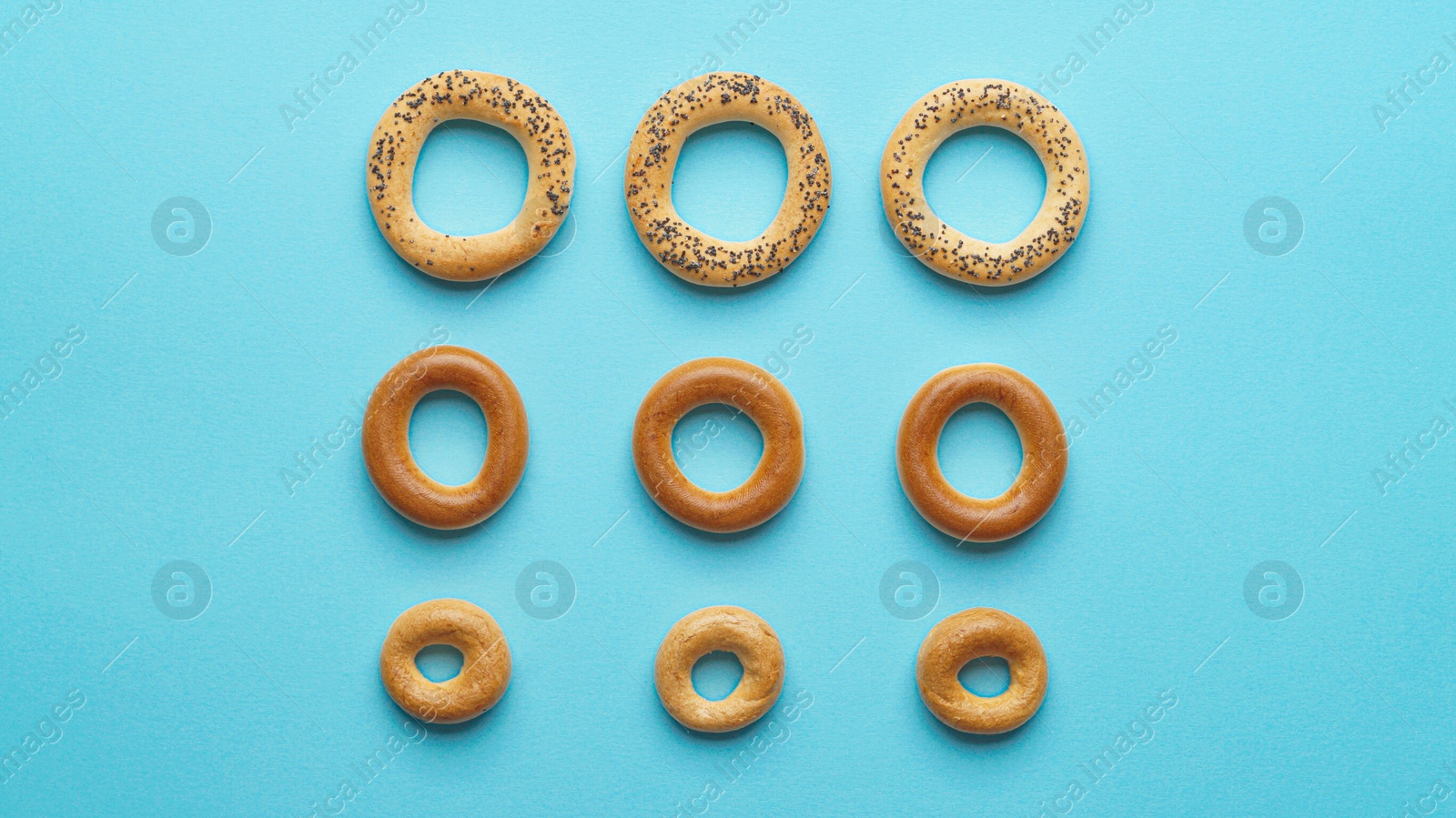 Photo of Many different delicious ring shaped Sushki (dry bagels) on light blue background, flat lay