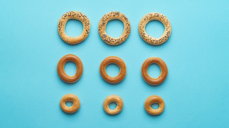 Photo of Many different delicious ring shaped Sushki (dry bagels) on light blue background, flat lay