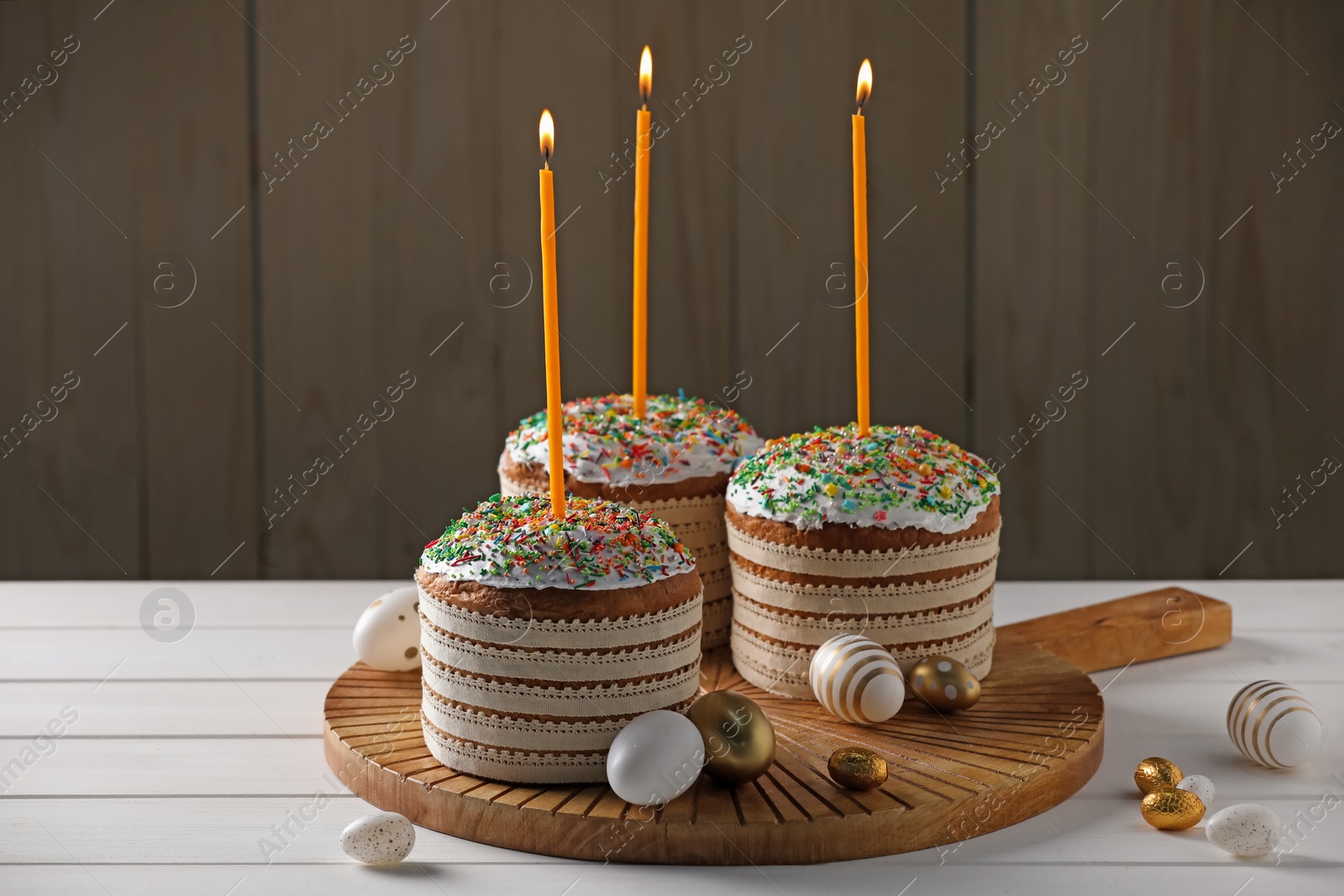 Photo of Traditional Easter cakes with sprinkles, candles and decorated eggs on white table. Space for text