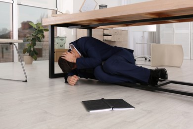 Photo of Scared man hiding under office desk during earthquake