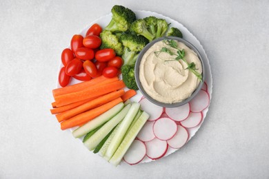 Plate with delicious hummus and fresh vegetables on light grey table, top view