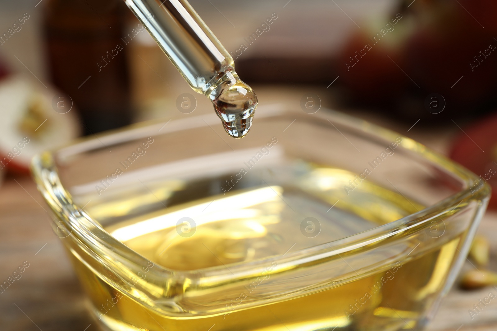 Photo of Dripping natural grape seed oil from pipette into bowl on wooden table, closeup. Organic cosmetic