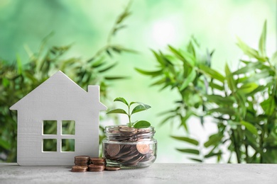 Photo of House model and jar with coins on table against blurred background. Space for text