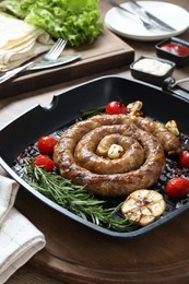Photo of Delicious homemade sausage with garlic, tomatoes, rosemary and spices in grill pan on wooden table