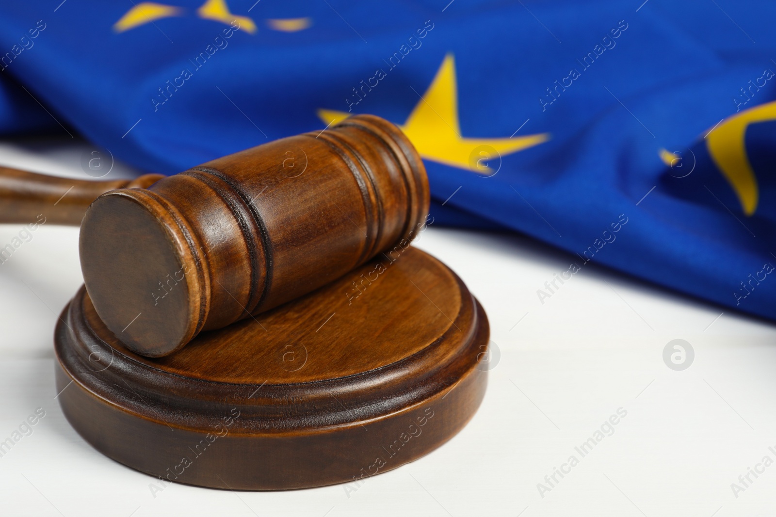 Photo of Wooden judge's gavel and flag of European Union on white table, closeup. Space for text