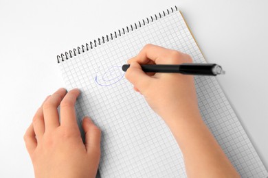 Photo of Child erasing doodle drawn with erasable pen in notepad against white background, top view