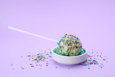 Photo of Delicious confectionery. Sweet cake pop and sprinkles on light violet background