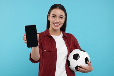 Photo of Happy fan holding soccer ball and showing smartphone on light blue background