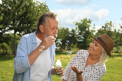 Photo of Lovely mature couple spending time together in park. Man blowing soap bubbles