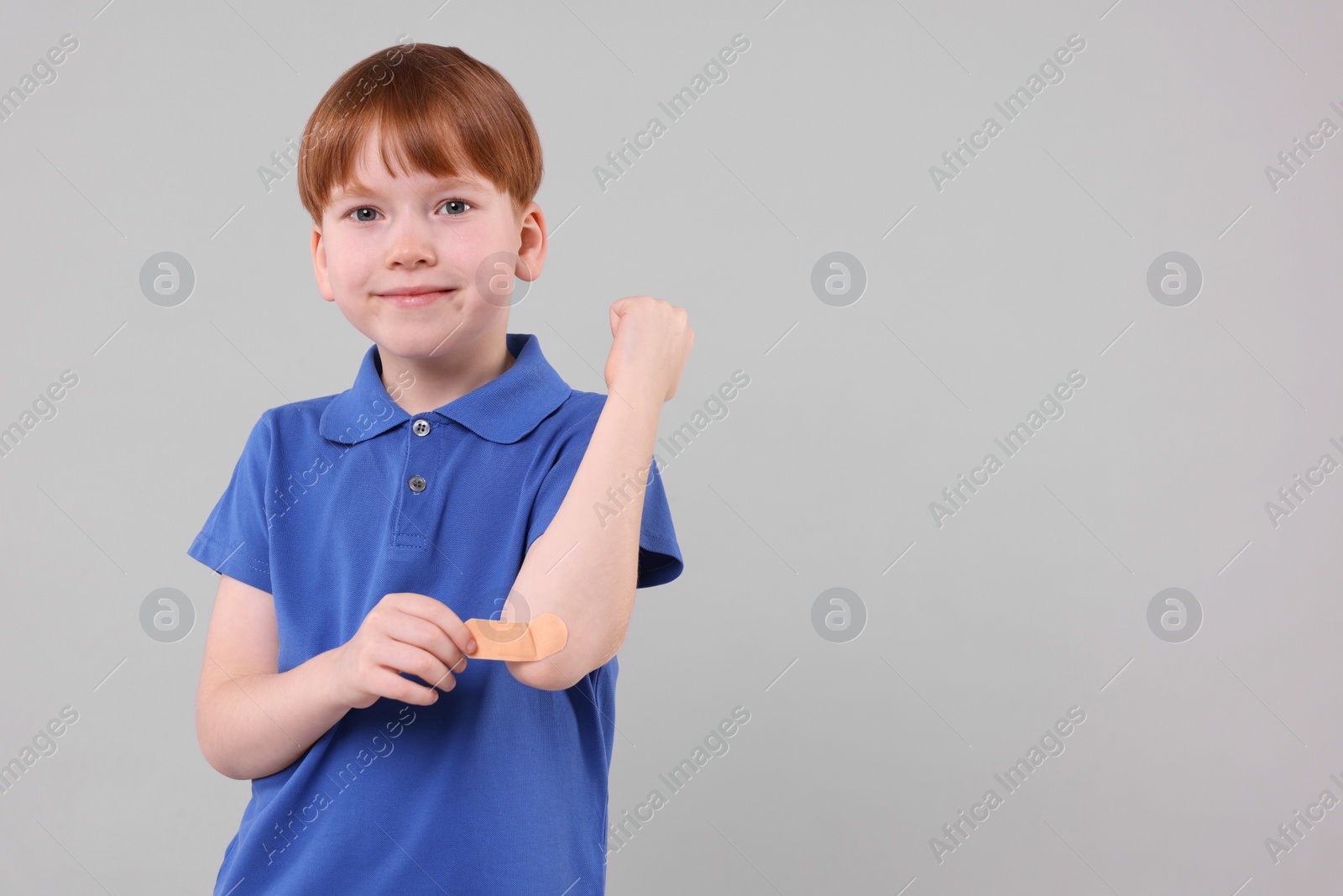 Photo of Little boy putting sticking plaster onto elbow against light grey background. Space for text