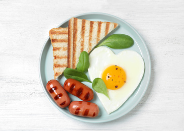 Plate of tasty breakfast with heart shaped fried egg  on white wooden table, top view