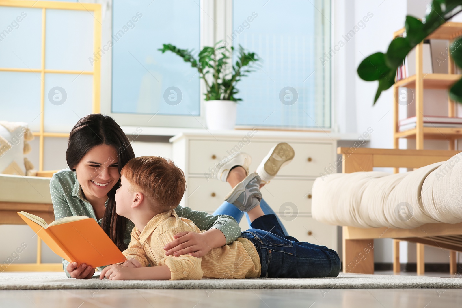 Photo of Mother reading book with her son on floor in living room at home