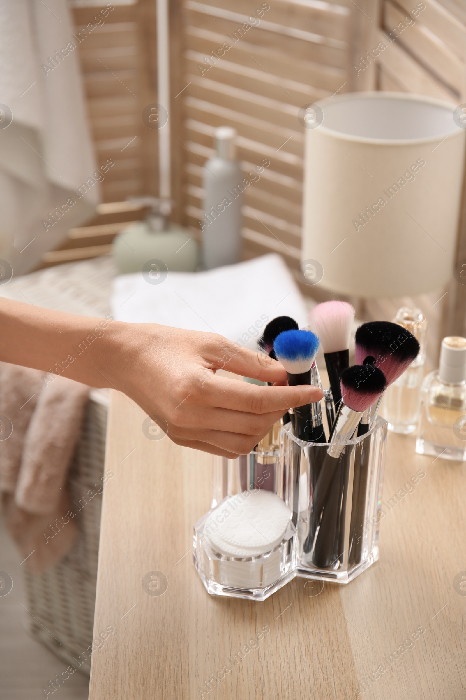 Photo of Woman taking brush from organizer for makeup cosmetic products on table