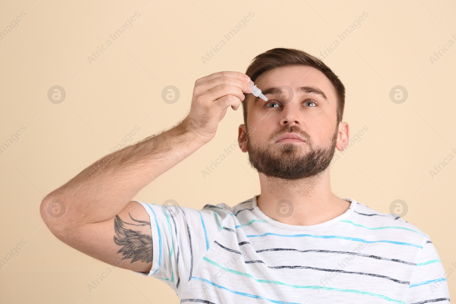 Photo of Young man using eye drops on beige background