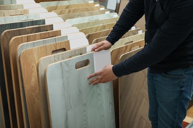 Photo of Man choosing wooden flooring among different samples in shop, closeup