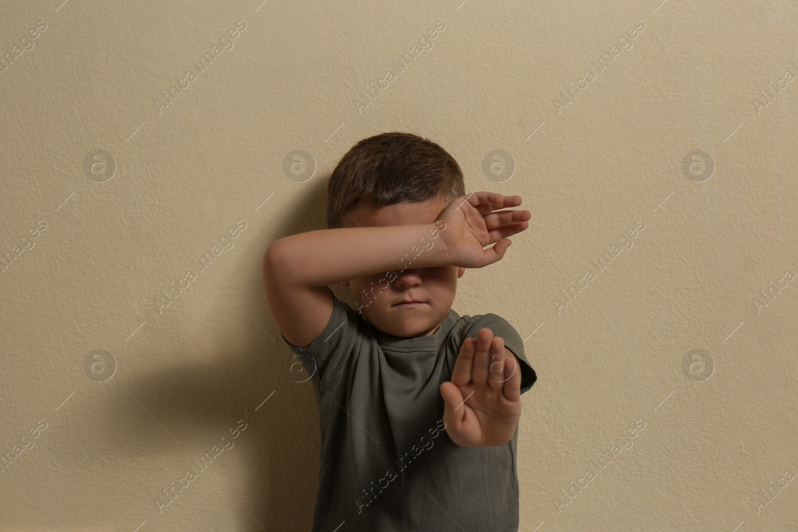 Photo of Scared little boy closing face with hand on yellow background. Child in danger