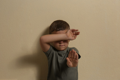 Scared little boy closing face with hand on yellow background. Child in danger