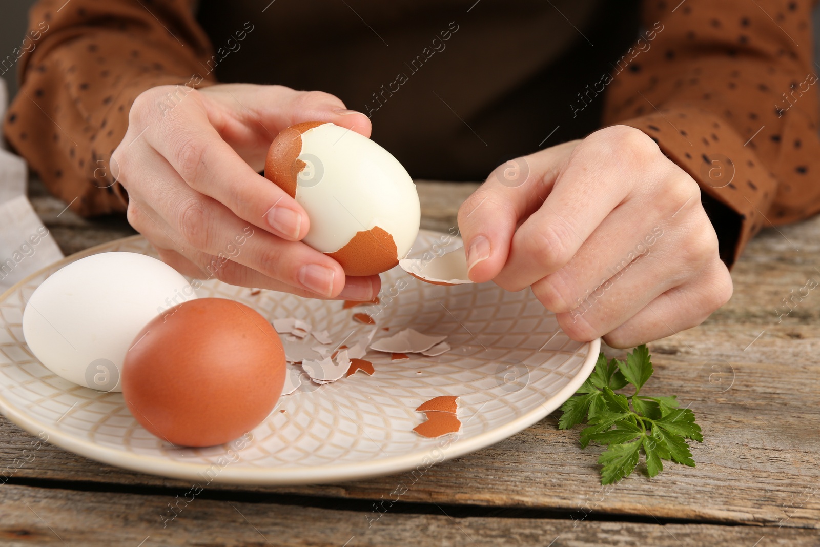 Photo of Woman peeling boiled egg at old wooden table, closeup