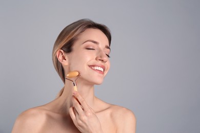 Young woman using natural jade face roller on light grey background