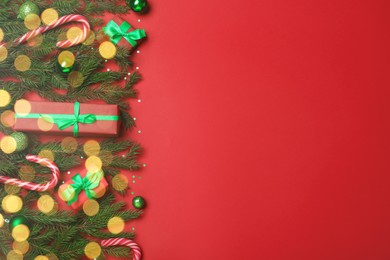 Photo of Flat lay composition with fir tree branches, Christmas decor and gift boxes on red background, space for text. Bokeh effect