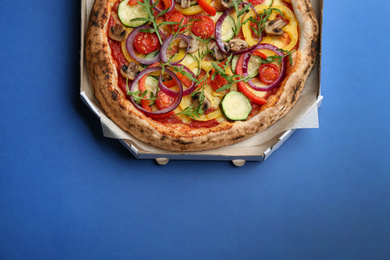Photo of Delicious vegetable pizza in cardboard box on blue background, top view. Space for text