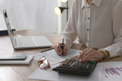 Photo of Tax accountant with calculator working at table in office, closeup