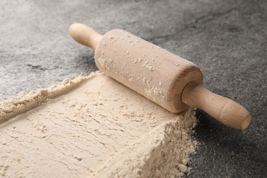 Photo of Scattered flour and rolling pin on grey textured table, closeup