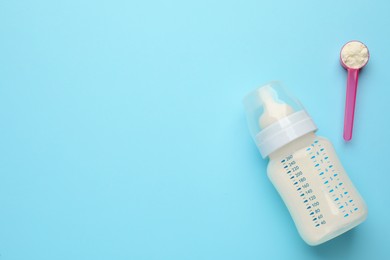 Feeding bottle with infant formula and powder on light blue background, flat lay. Space for text