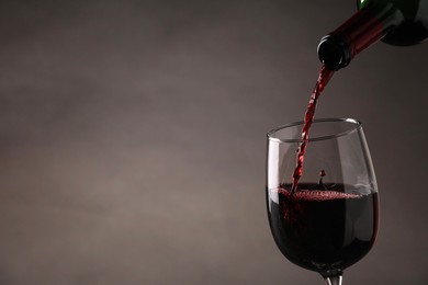 Pouring tasty red wine from bottle into glass on gray background, closeup. Space for text