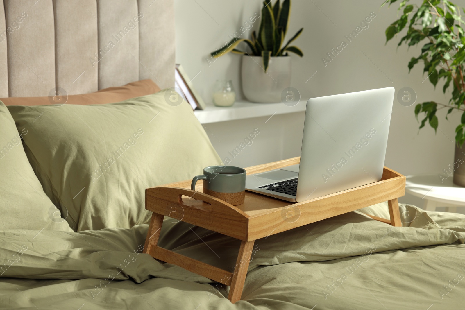 Photo of Wooden tray with modern laptop and cup of aromatic tea on bed indoors