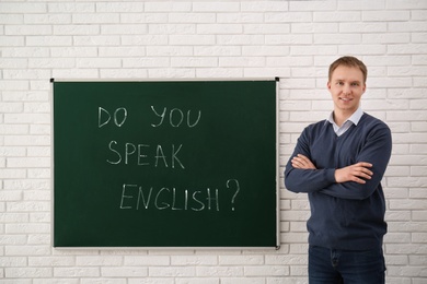 Photo of Teacher near green chalkboard with inscription Do You Speak English? in classroom