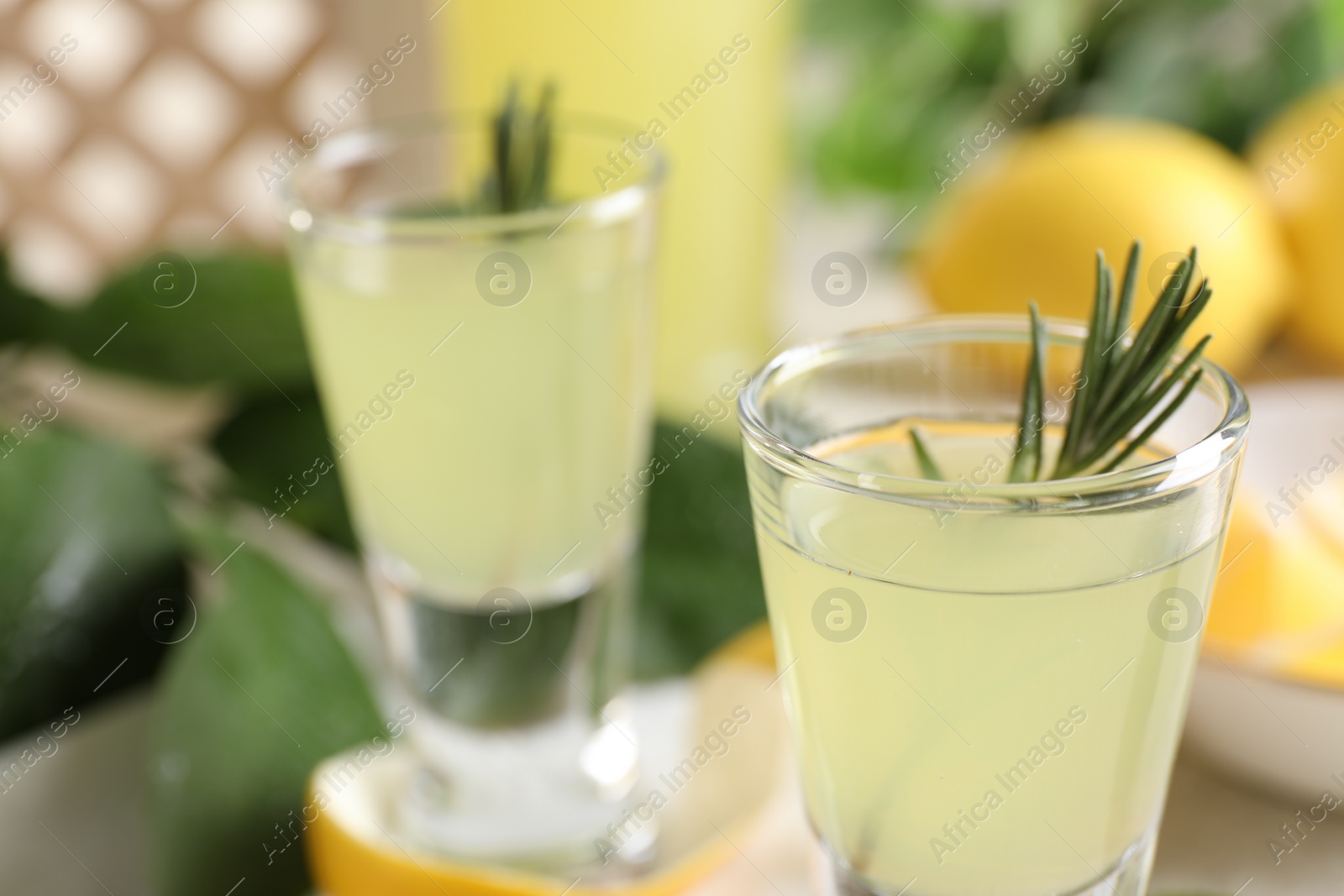 Photo of Tasty limoncello liqueur with rosemary on table, closeup. Space for text