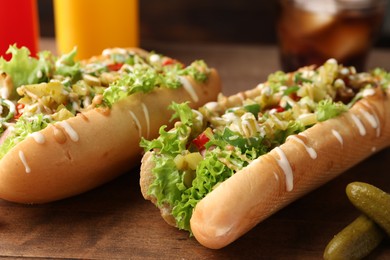 Tasty hot dogs with chili, lettuce, pickles and sauces on wooden table, closeup