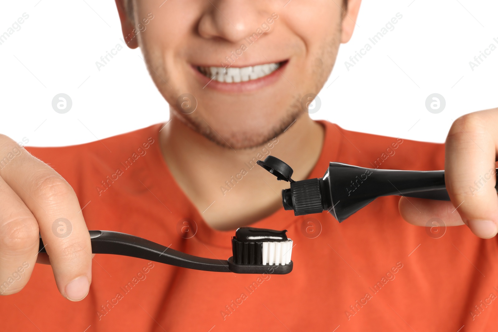 Photo of Man applying charcoal toothpaste onto toothbrush on white background, closeup