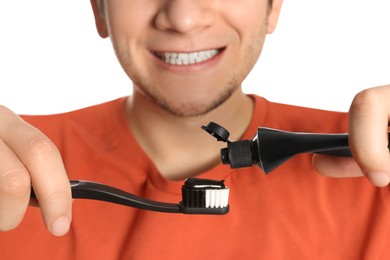 Photo of Man applying charcoal toothpaste onto toothbrush on white background, closeup