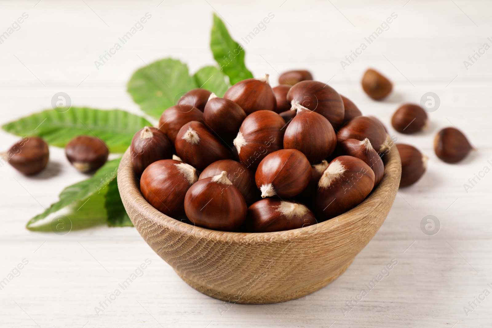 Photo of Fresh sweet edible chestnuts in bowl on white wooden table, closeup