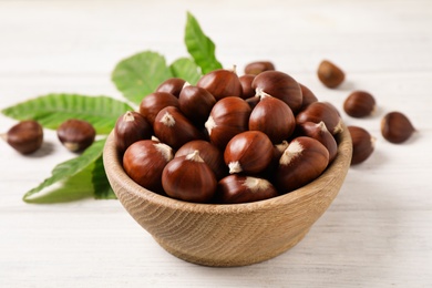 Fresh sweet edible chestnuts in bowl on white wooden table, closeup