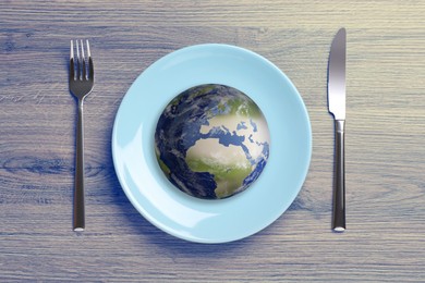 Image of Global food crisis concept. Globe of Earth in plate and cutlery on wooden table, flat lay