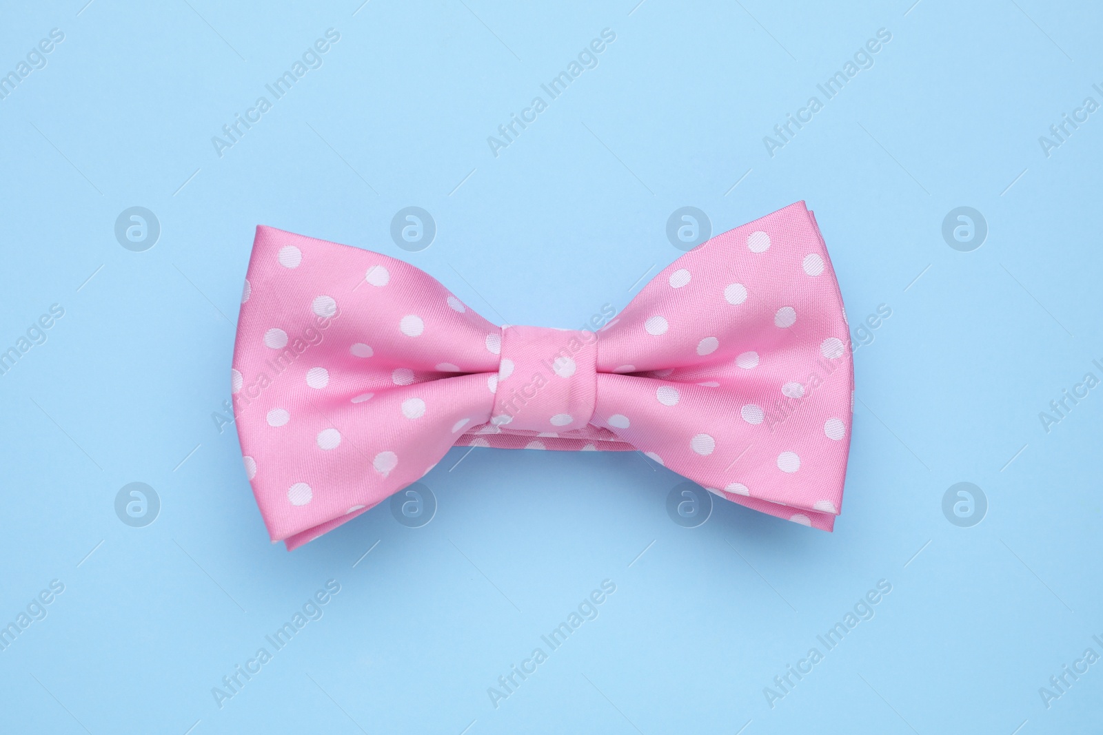 Photo of Stylish pink bow tie with polka dot pattern on light blue background, top view
