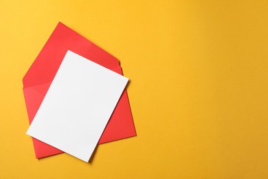 Photo of Blank sheet of paper and letter envelope on orange background, top view. Space for text