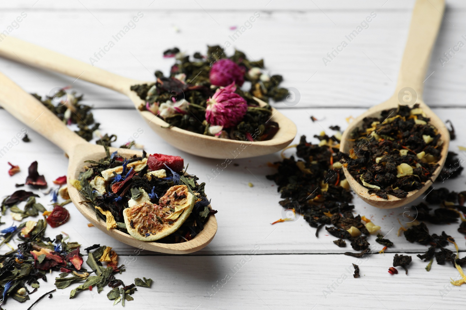 Photo of Spoons with dried herbal tea leaves and fruits on white wooden table, closeup