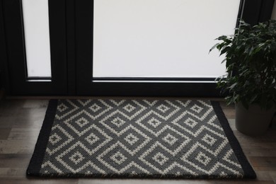 Photo of New clean door mat with pattern and beautiful houseplant on floor near entrance