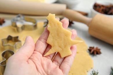 Photo of Woman holding unbaked Christmas tree shaped cookie at table, closeup